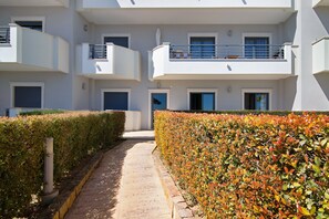 A multi-story residential building with balconies, a pathway, and neatly trimmed hedges.