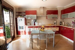Une cuisine moderne avec des meubles de rangement rouges, une table à manger avec des chaises et un four à micro-ondes.