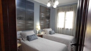 A hotel room with two beds, a nightstand with a lamp, a large artwork on the wall, and a window with curtains. - Holiday Home "Casa Montelucía" with Mountain View, Terrace & Wi-Fi (Montecorto)