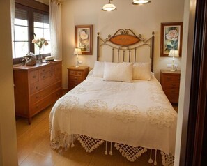 Une chambre à coucher bien rangée, avec un lit, une commode, des tables de chevet et des œuvres d’art encadrées accrochées aux murs.