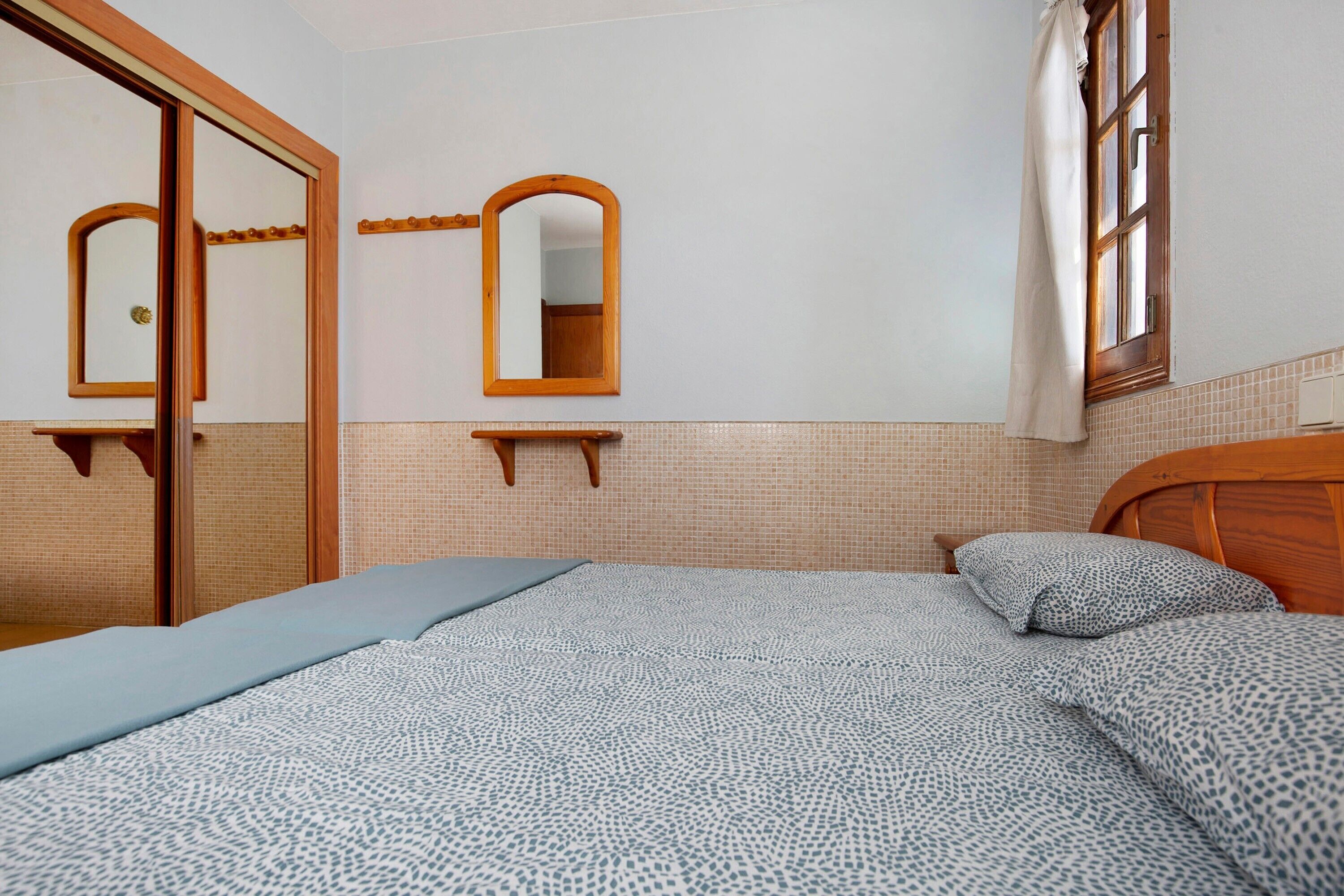 Une chambre à coucher avec un lit, un miroir, une fenêtre et une porte.