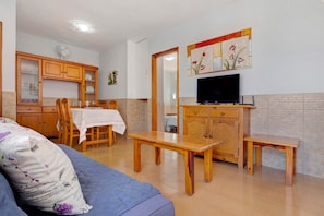 Sala de estar com sofá, mesa de jantar de madeira, televisão e armários.