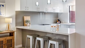 A modern kitchen with white cabinets, a central island with stools, and pendant lighting. - CONVENIENTLY LOCATED 250M (APPROX) TO THE EXQUISITE SHORES OF GEOGRAPHE BAY (Dunsborough)