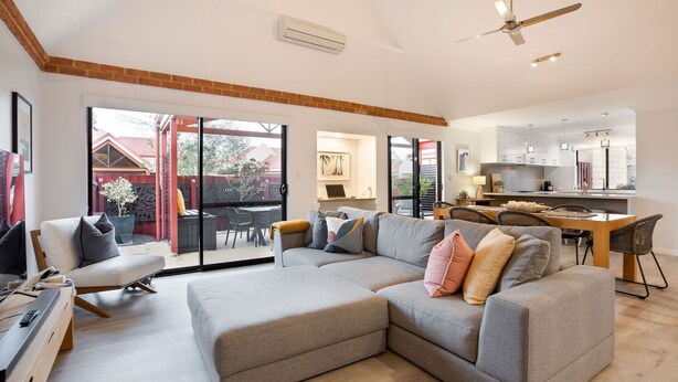 A spacious living area with a large grey sectional sofa, a wooden coffee table, and a TV stand. A dining area with a table and chairs is visible in the background. - CONVENIENTLY LOCATED 250M (APPROX) TO THE EXQUISITE SHORES OF GEOGRAPHE BAY (Dunsborough)