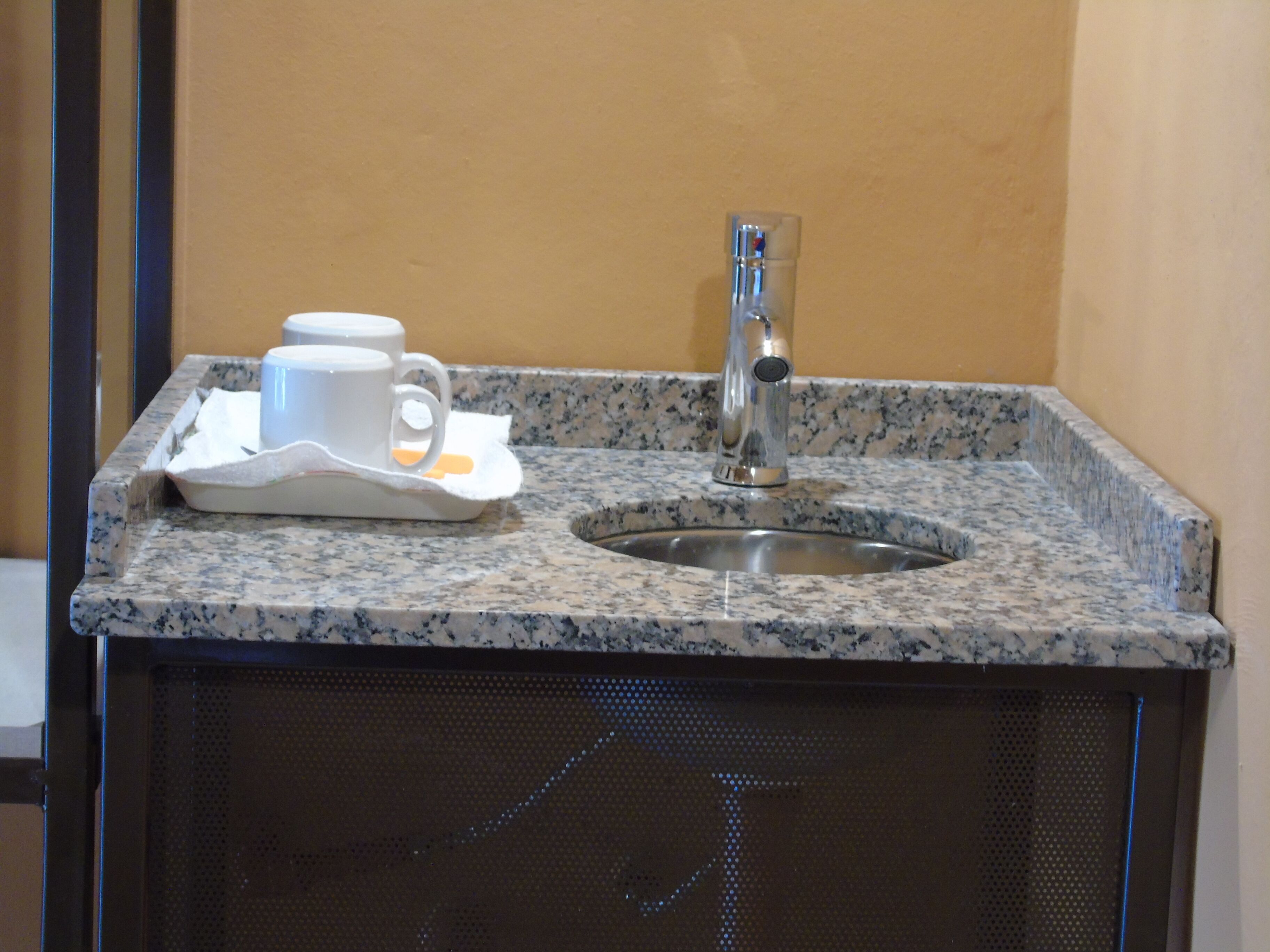 Un plan de travail en granit avec un évier, un robinet et un plateau contenant une tasse et un savon.