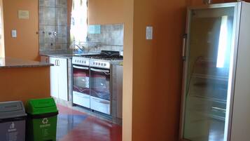 Una cocina con estufa, horno y refrigerador. Hay dos contenedores de basura, uno etiquetado 'Basura' y el otro 'Reciclables'.