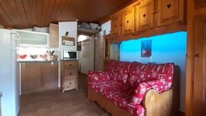 Una habitación acogedora con techo de madera, un sofá rojo con funda estampada, un armario de madera y un microondas.