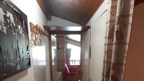 Un pasillo estrecho con vigas de madera en el techo, un radiador y una cama roja a la derecha.