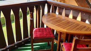 Una terraza de madera con una mesa redonda y dos sillas rojas con cojines.