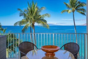 Ein Balkon mit zwei Korbstühlen und einem Tisch, mit Blick auf das klare, blaue Meer und Palmen.