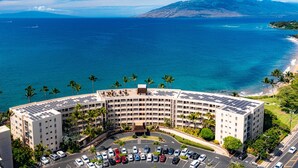 A hotel with a curved building, a parking lot, and a view of the ocean and mountains. - TOP FLOOR-STUNNING OCEAN VIEWS-WELL EQUIPPED-ALL NEW FURNISHINGS (Kihei)