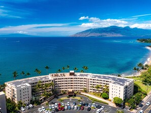 A hotel with a curved building, a parking lot, and a view of the ocean and mountains.