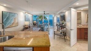 A modern kitchen with a granite countertop, a Bosch dishwasher, and a view to a balcony with a palm tree. - TOP FLOOR-STUNNING OCEAN VIEWS-WELL EQUIPPED-ALL NEW FURNISHINGS (Kihei)