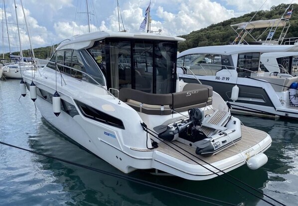 Un yate a motor blanco con zona de estar cubierta y una tabla para wakeboard en la cubierta.