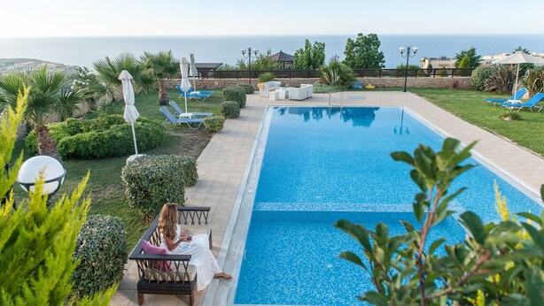 Un espace piscine avec vue sur la mer, entouré de verdure et agrémenté de chaises longues.
