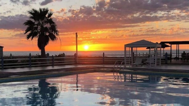 En swimmingpool med udsigt til solnedgang, en palme og en redningsplatform.