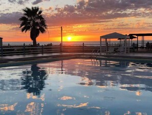 Una piscina con vista al atardecer, una palmera y un puesto de salvavidas.