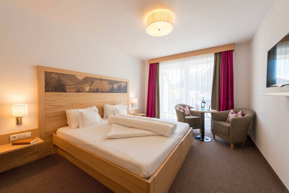 A hotel room with a large bed, a desk with a chair, a television, and a window with curtains.