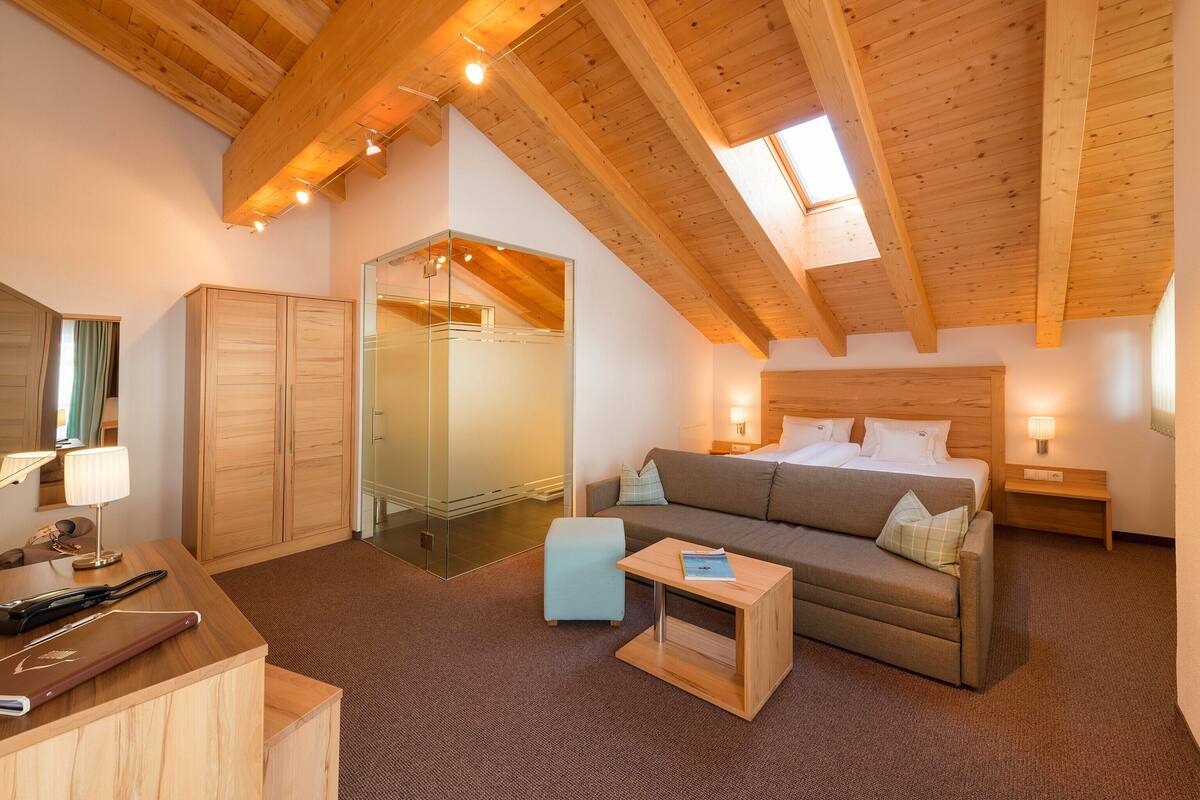 A hotel room with a wooden ceiling, a bed, a sofa, a small table, a desk, and a wardrobe.