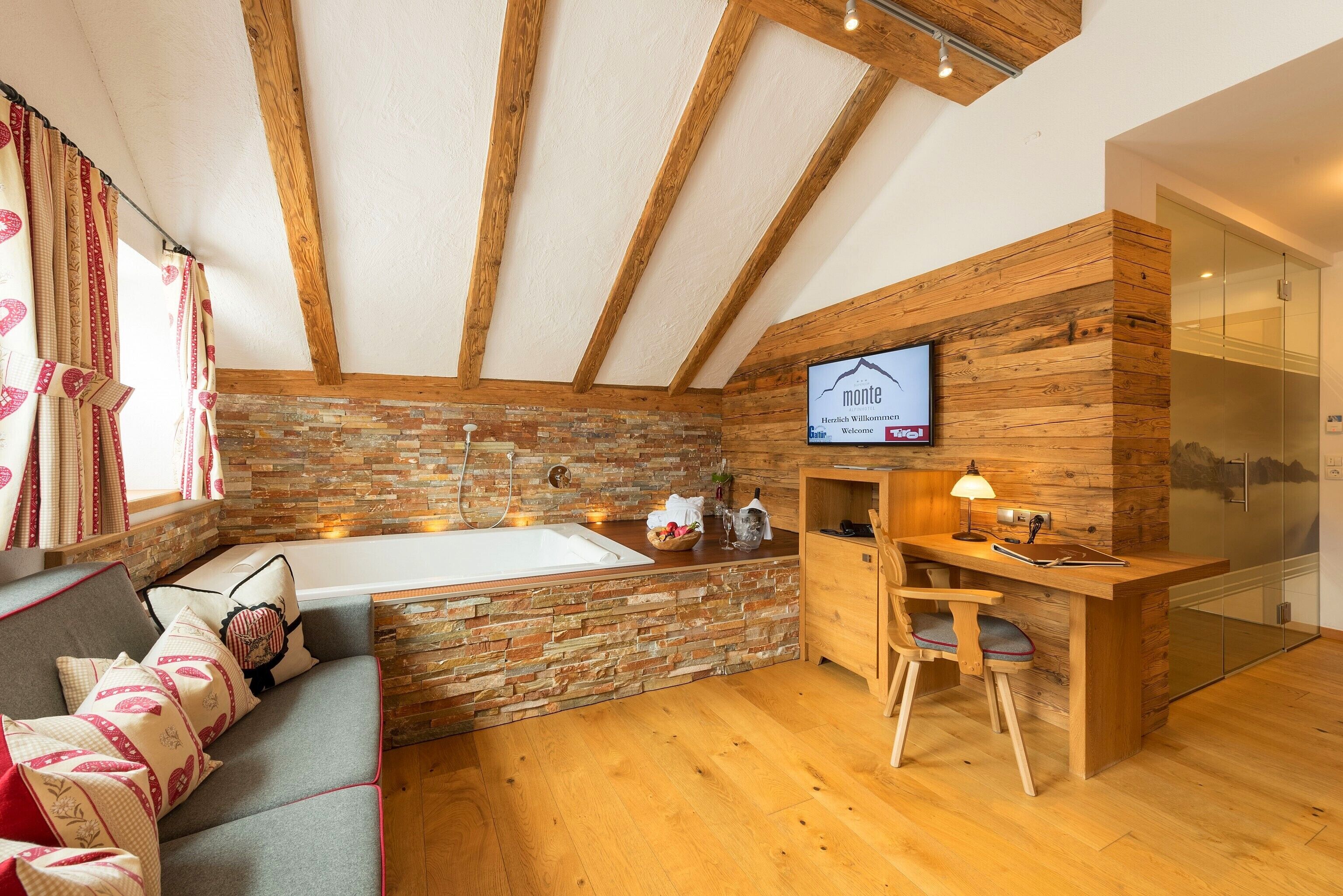 Ein modernes Badezimmer mit einer Steinwand, Holzbalken an der Decke, einer Badewanne und einem Holzwaschtisch mit Waschbecken und Spiegel.