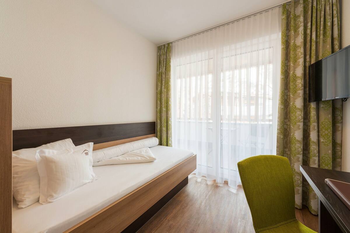 A hotel room with a bed, a desk, a chair, and a TV.
