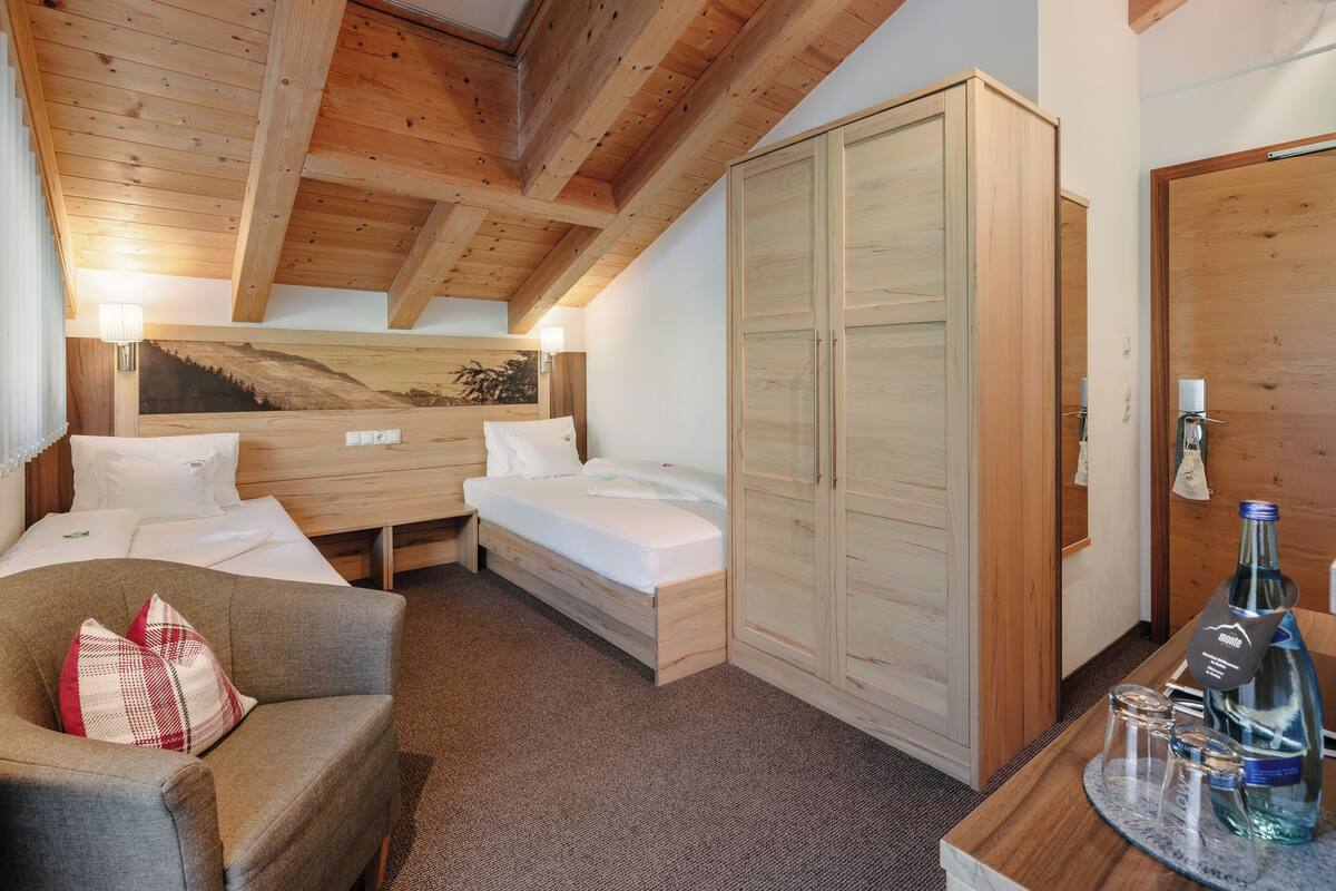 A wooden-paneled room with a bed, a sofa, a wardrobe, and a small table with bottles and glasses.