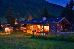 Ein rustikales Berglodge mit überdachter Veranda und Essbereich, umgeben von Bäumen und einer Bergkulisse.
