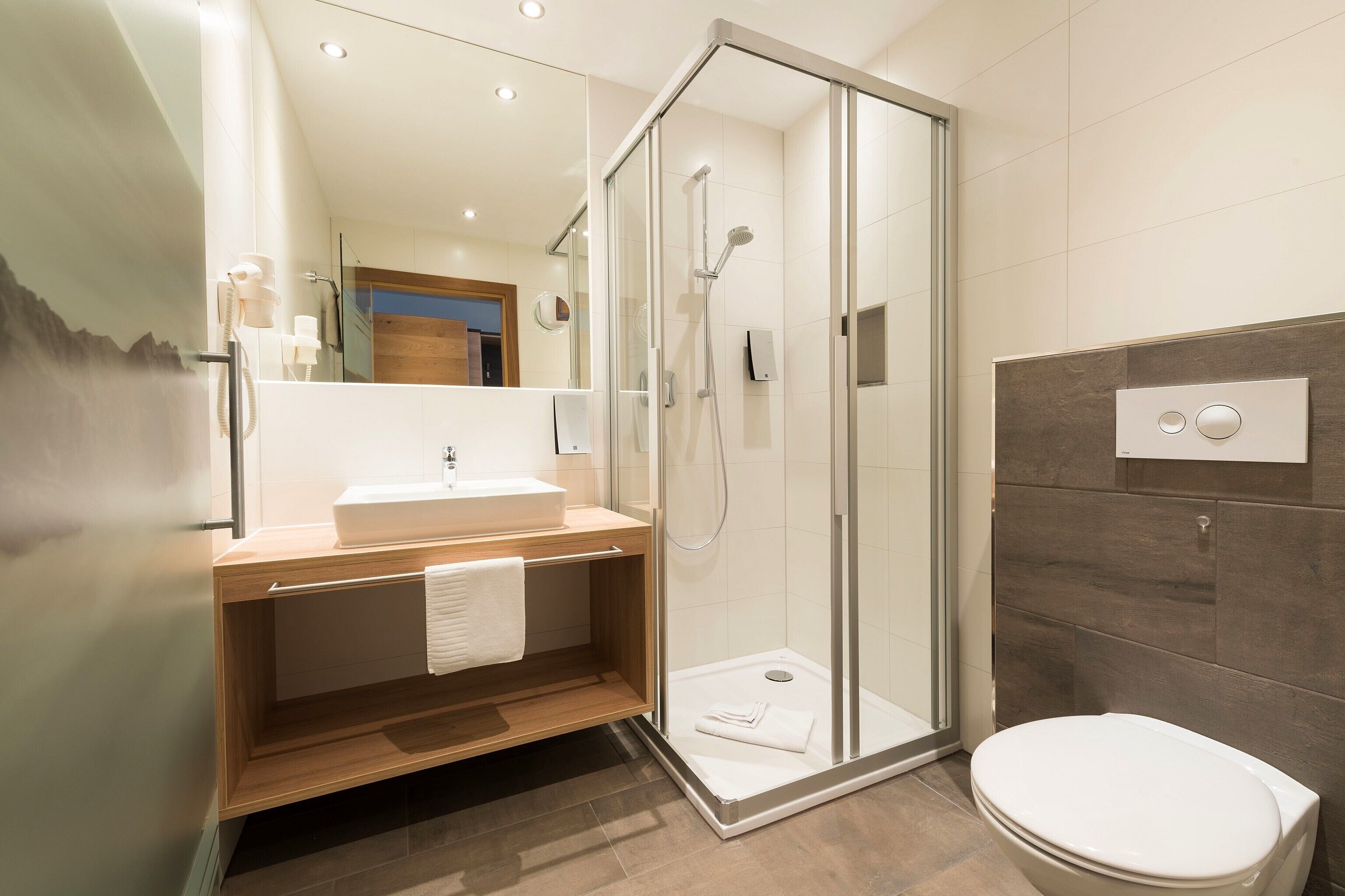 A modern bathroom with a glass-enclosed shower, a wooden vanity, a white sink, and a toilet.
