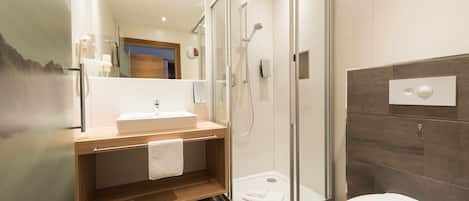 A modern bathroom with a glass-enclosed shower, a wooden vanity, a white sink, and a toilet.