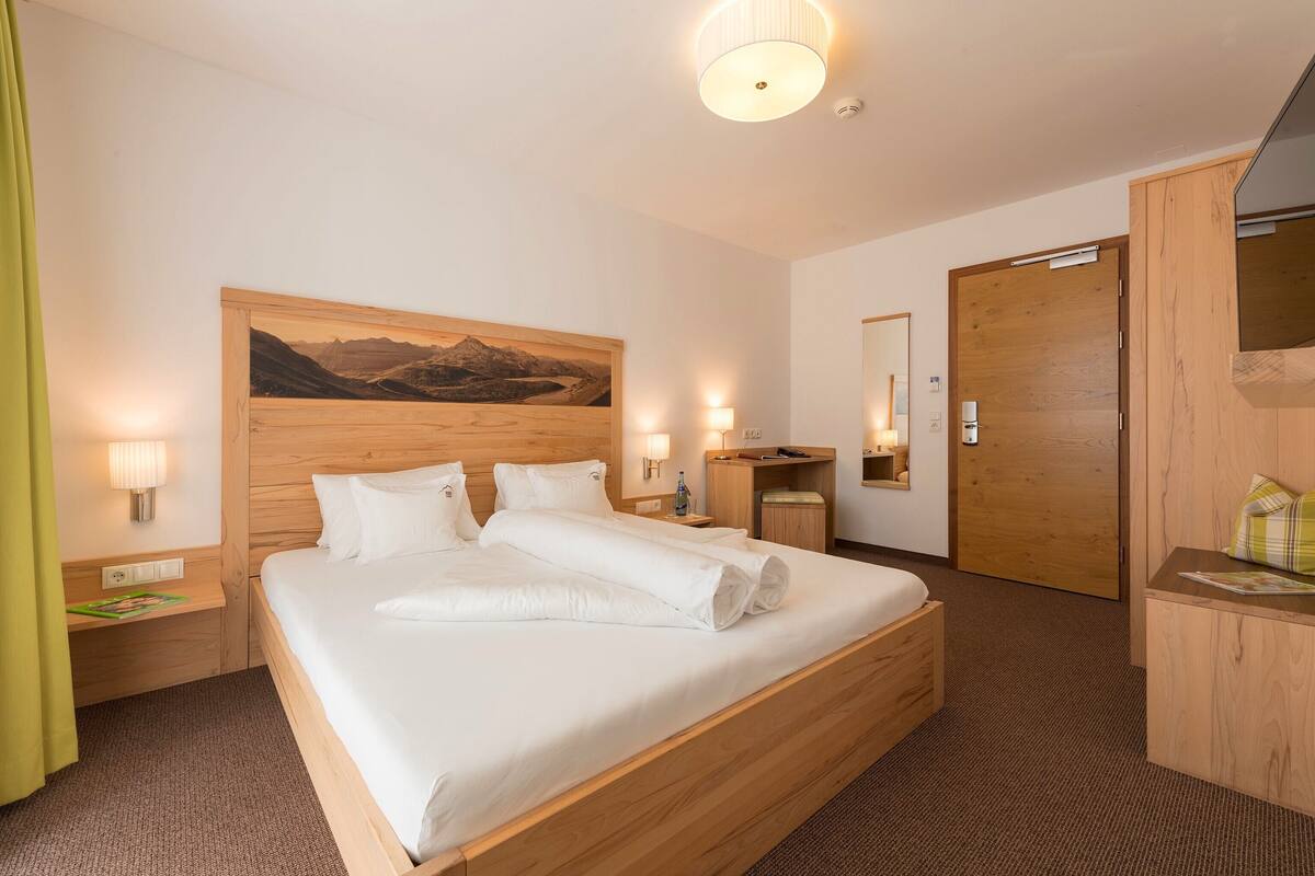 A hotel room with a large bed, wooden headboard, a painting on the wall, a wooden desk, and a mirror.