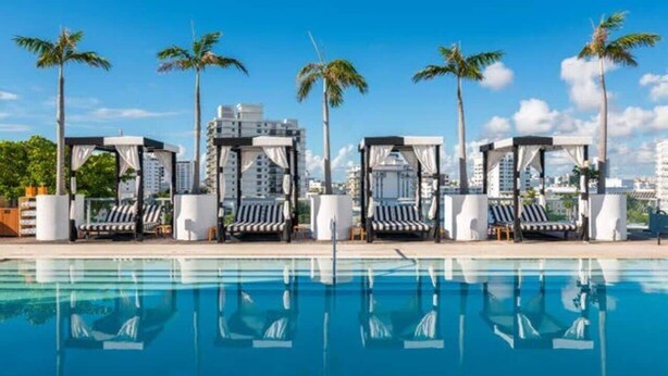 Una piscina con sillas de descanso y palmeras, rodeada de edificios.