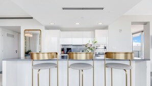 Una cocina moderna con armarios blancos, una isla central con tres taburetes de bar y un espejo grande.