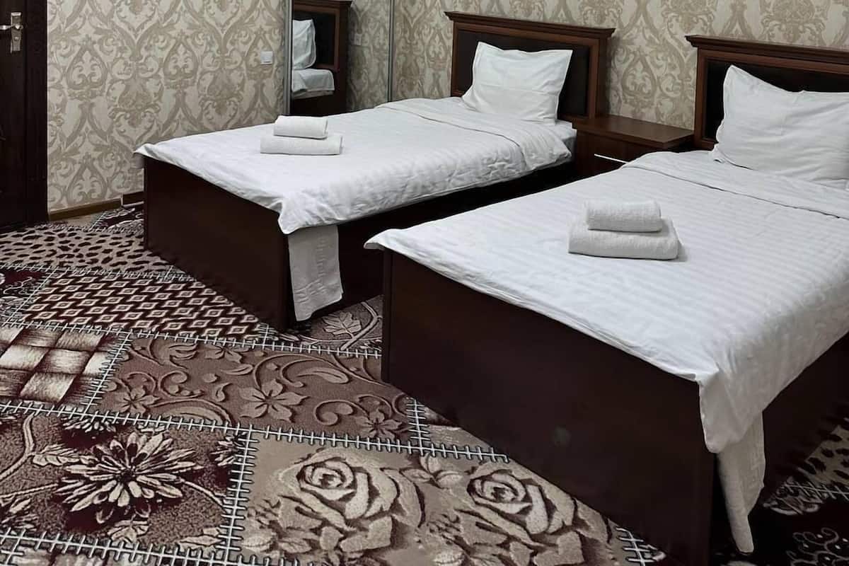 A hotel room with two beds, a chandelier, patterned wallpaper, and a large mirror.