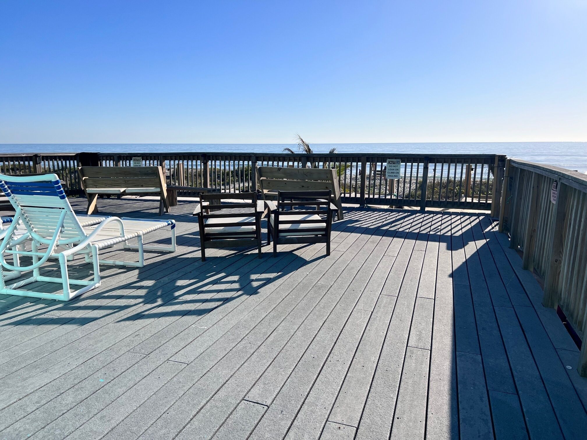 A wooden deck with benches and a lounge chair overlooking the ocean.