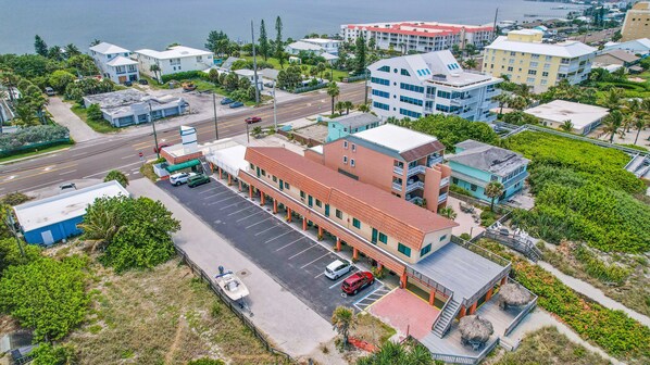 An aerial view of a coastal hotel with a parking lot, a beachside deck, and a view of the sea.