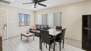 Una sala de estar moderna con sofá, mesa de comedor, sillas, ventilador de techo y refrigerador.