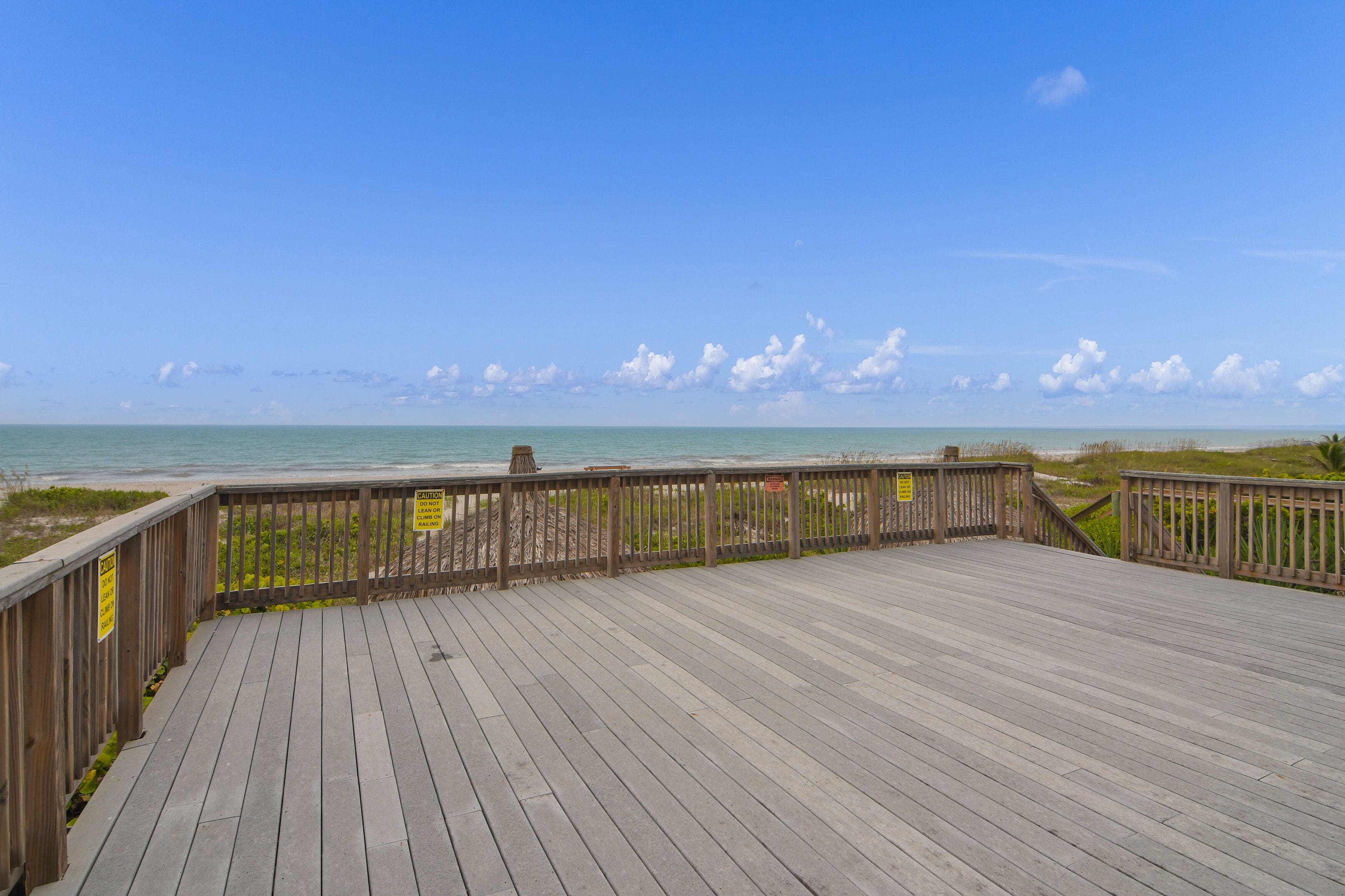 A wooden boardwalk leading to a beach with clear skies and distant clouds.