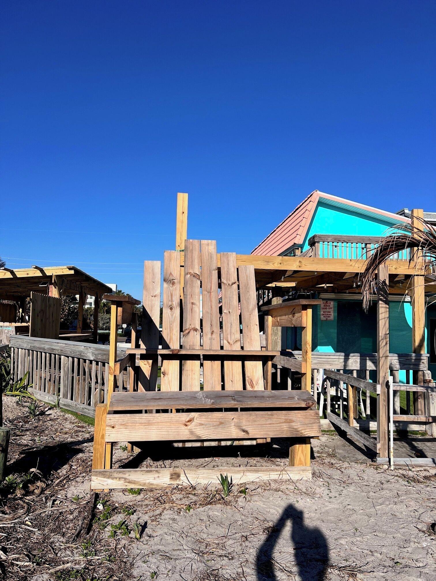 A wooden structure with a bench, surrounded by a wooden fence and a building with a blue roof.