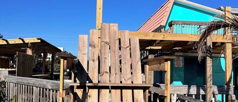 A wooden structure with a bench, surrounded by a wooden fence and a building with a blue roof.