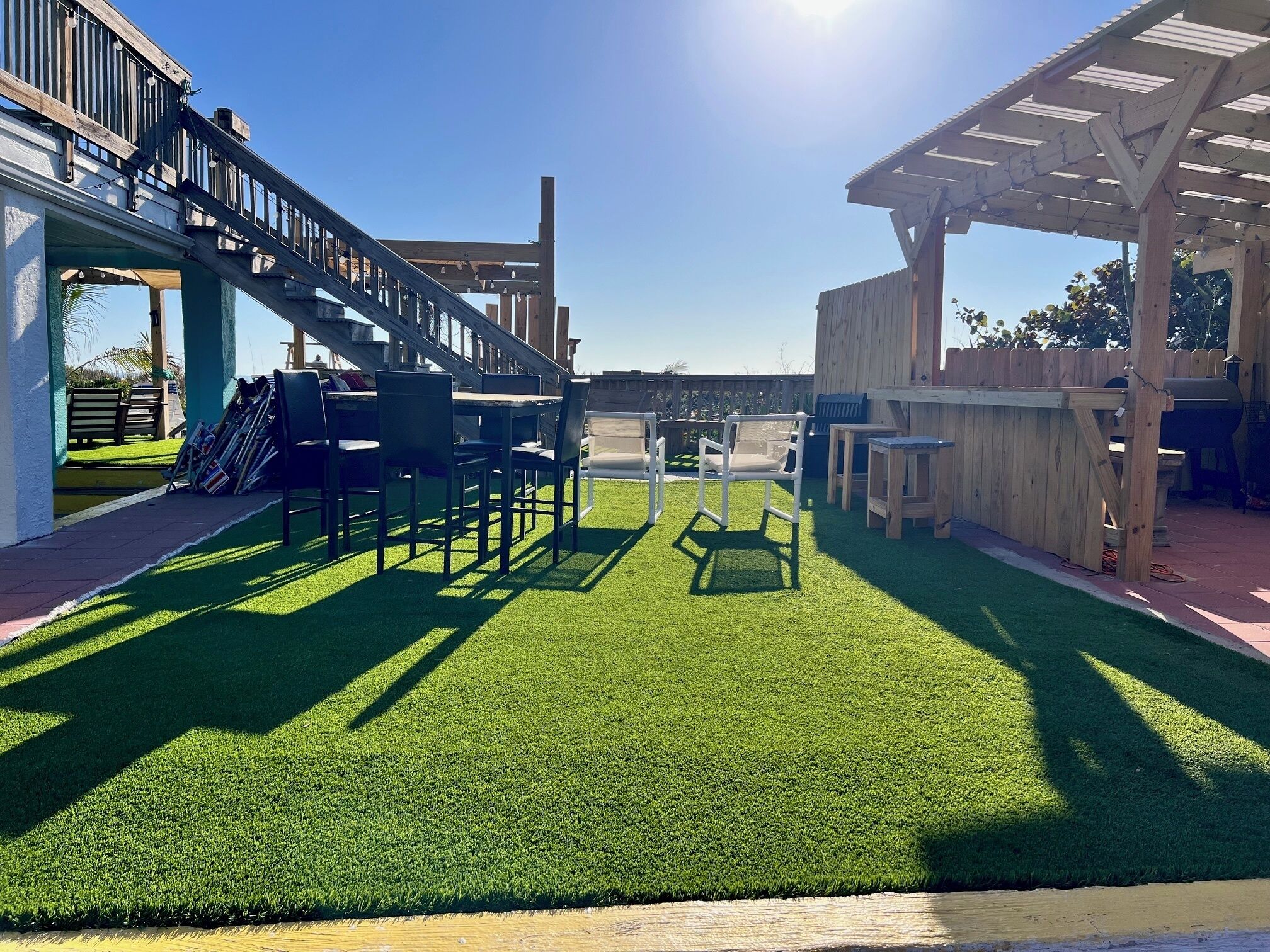 Un área de patio con césped artificial, mobiliario de madera y una estructura de pérgola.