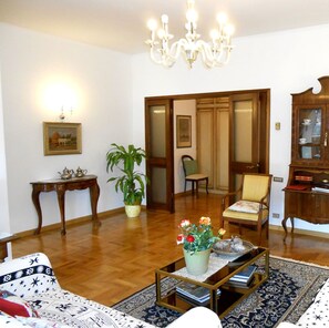 Una sala de estar con candelabro, un aparador de madera, un sofá, una mesa de centro con libros y una planta en maceta.