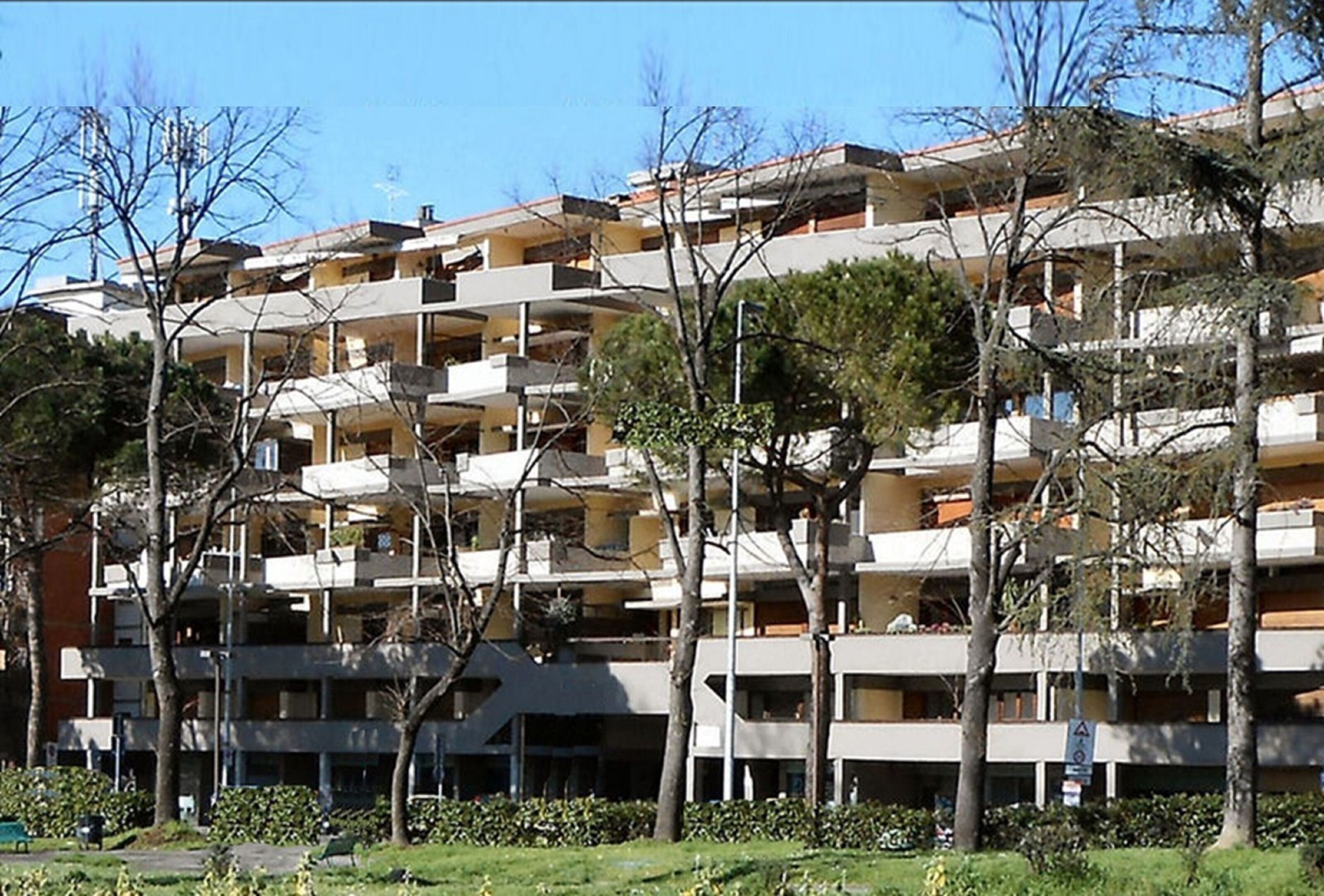 Een meerhoog appartementencomplex met balkons, omgeven door bomen en een gazon.