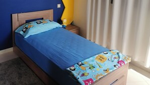 Une chambre à coucher avec un lit, une table de chevet, un mur décoré de motifs jaunes et bleus, et une fenêtre avec des rideaux.