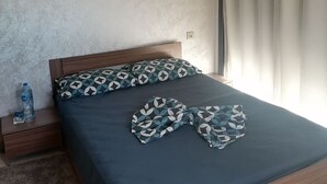 Une chambre à coucher avec un lit, une table de chevet, une bouteille d’eau et un rideau.