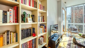 A modern living room with a large bookshelf filled with books, a flat-screen TV, and a comfortable seating area with a view of the city.