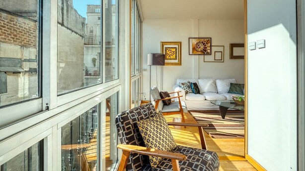A modern living room with a large window, a sofa set, and a patterned armchair.