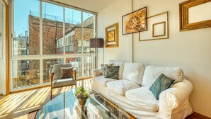 A modern living room with a large glass window, white sofa, and decorative frames on the wall.