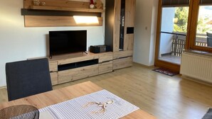 Ein Wohnzimmer mit Fernseher, Holzmöbeln und einem Balkon mit Blick.
