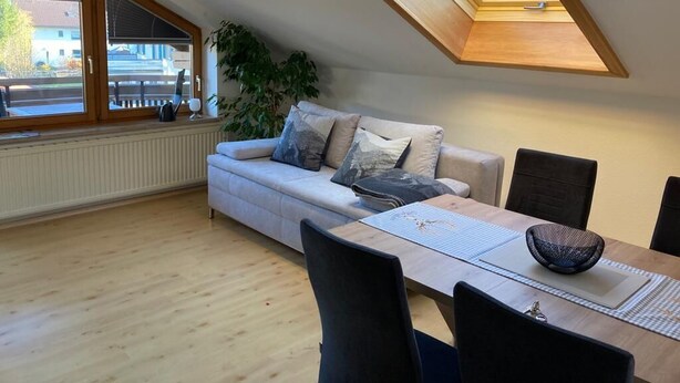 Ein Loft-Zimmer mit hoher Decke, einem Oberlicht, einer Couch, einem Esstisch und Blick ins Freie.