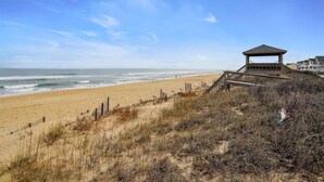 Een strand met een houten constructie, zandduinen en een heldere lucht.